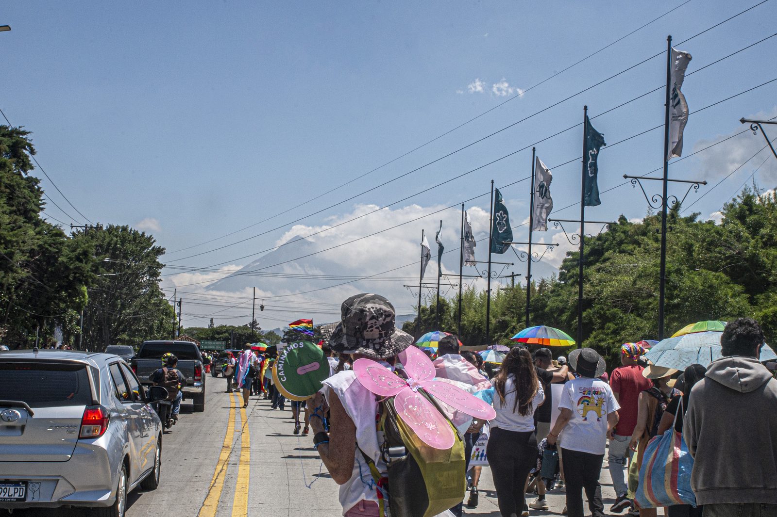 Persona del equipo de seguridad con alas de mariposa rosadas, caminando por la carretera con el volcán de fondo