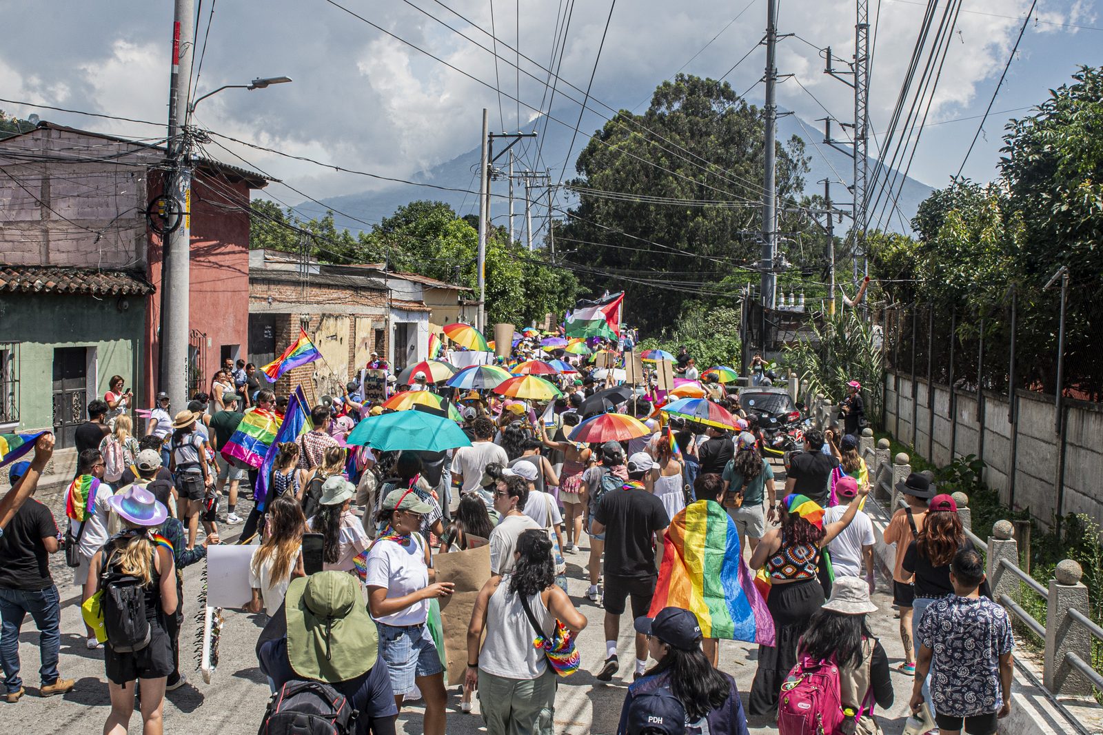 Multitud con sombrillas arcoíris caminando por Antigua, con el volcán de fondo